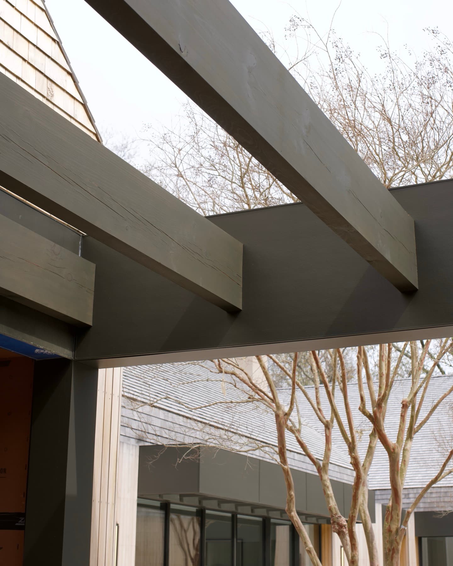 New pressure-treated deck joists in the foreground with a cedar-shingled house wrapped in weather barrier behind