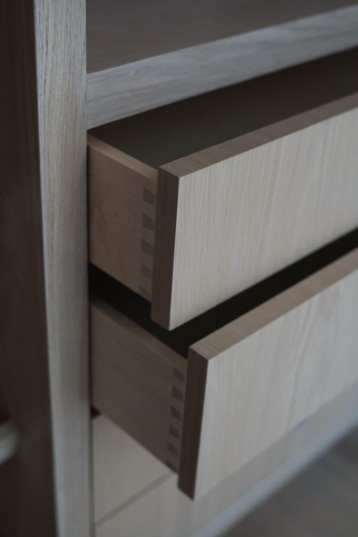Underside view of two white oak drawer boxes showing dovetail pins and walnut-toned edge banding