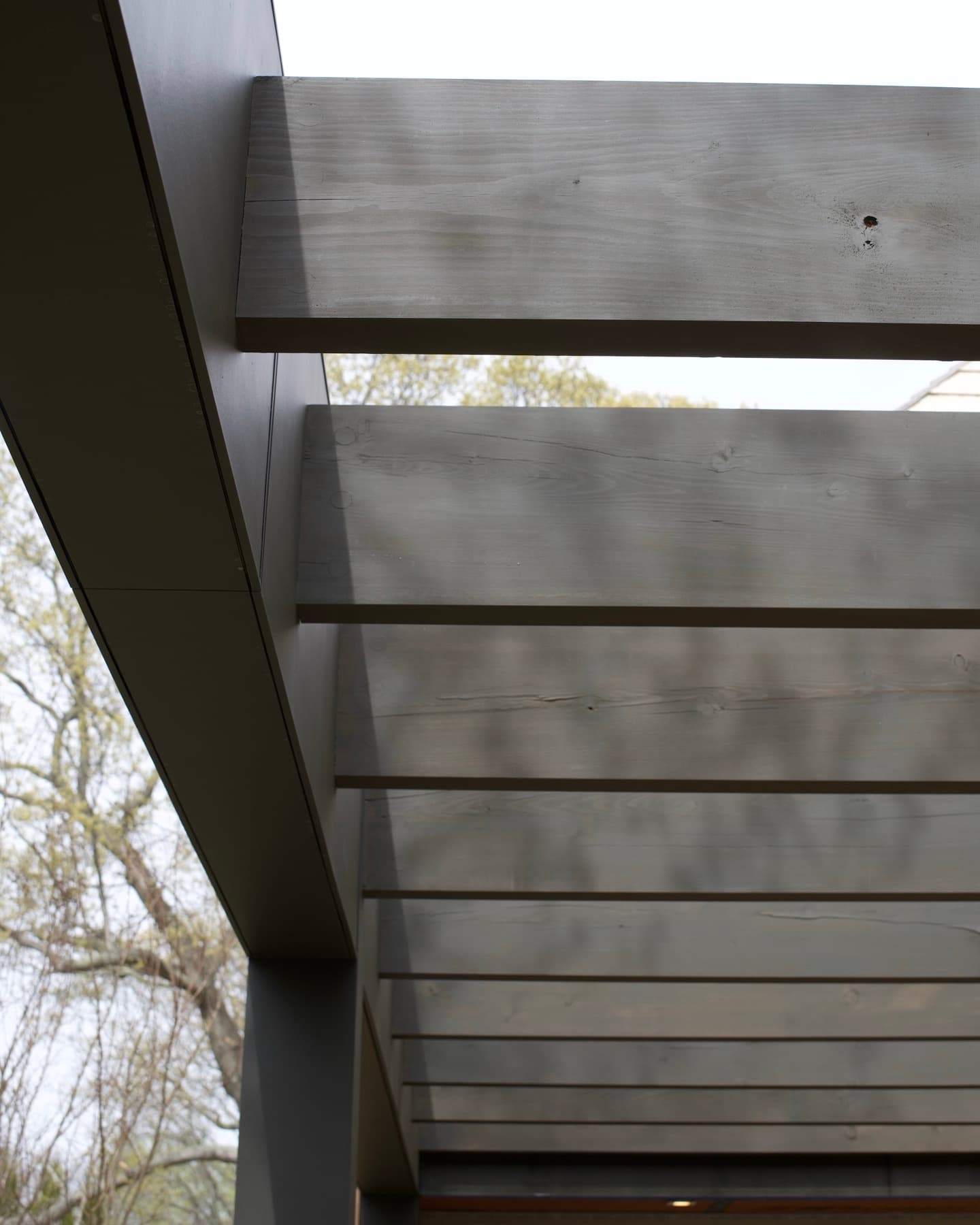 Underside of a gray-stained pergola with evenly spaced rafters over a steel-wrapped beam