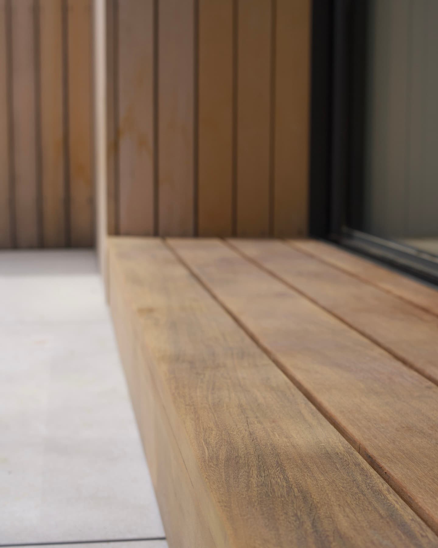 Wide wood step and vertical slat cladding meeting a pale stone patio at a sliding glass door