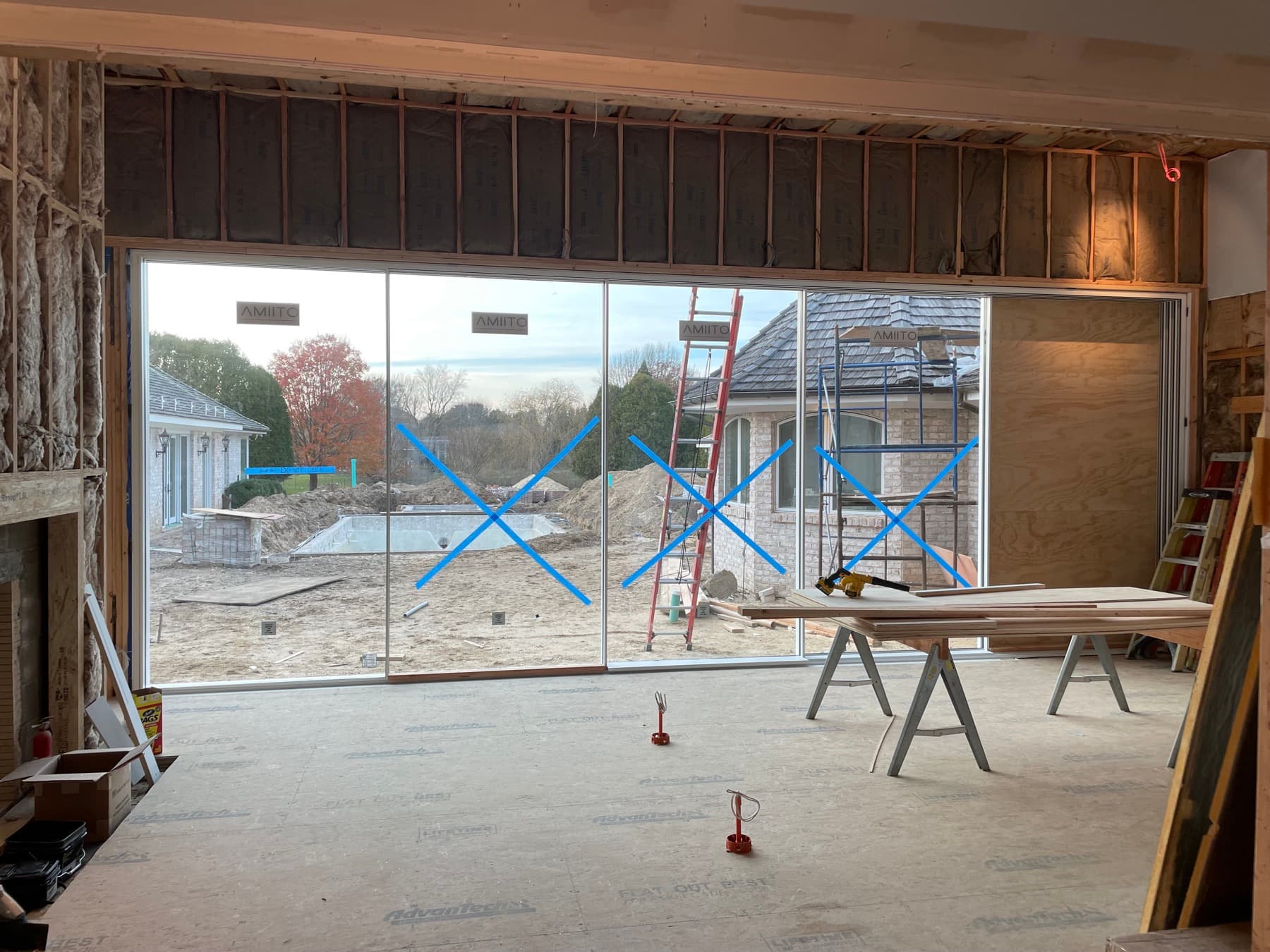 Floor-to-ceiling glass wall panels newly installed in a framed great room, taped with protective X marks