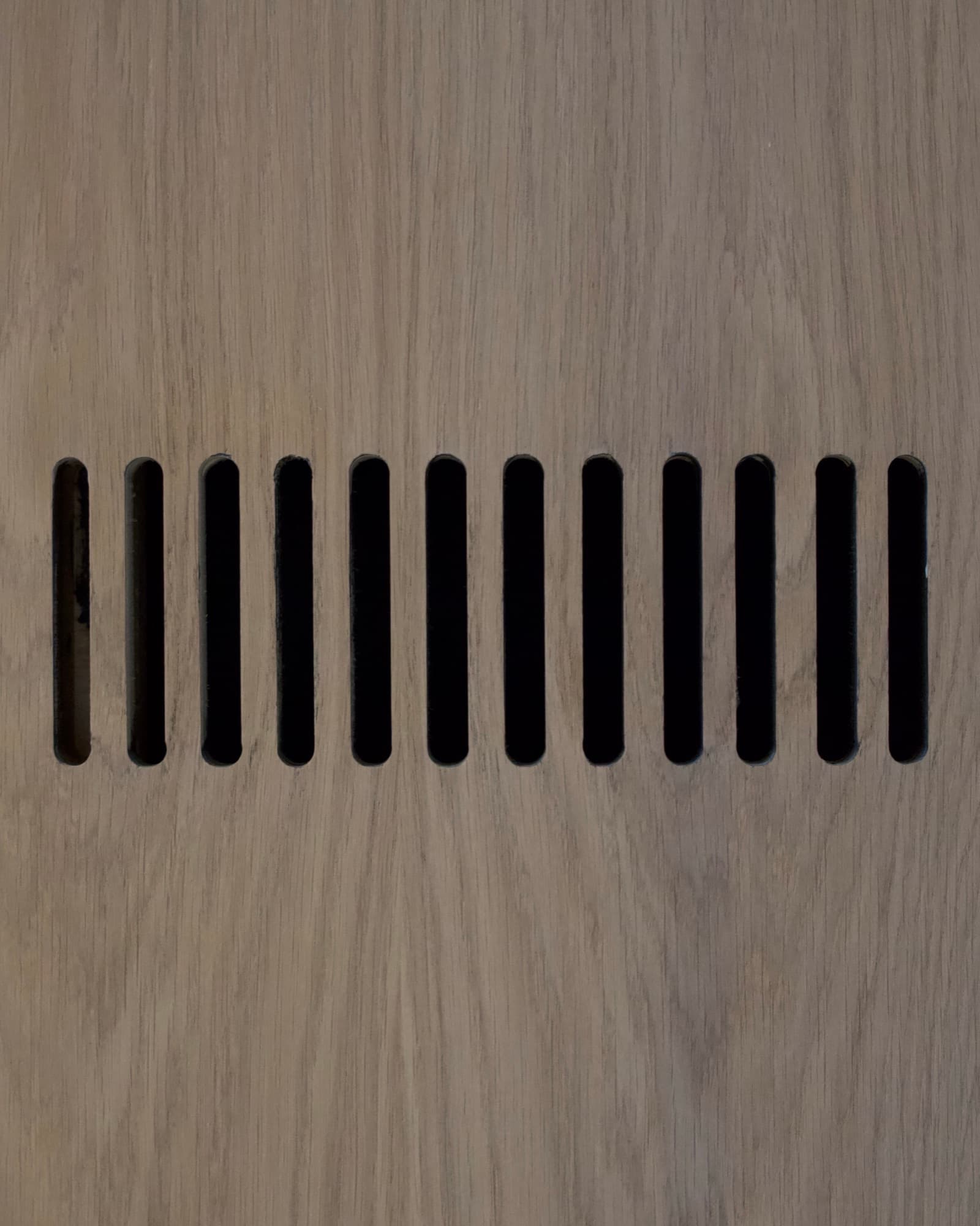 Close-up of a row of slotted vent openings routed cleanly into a white oak cabinet panel