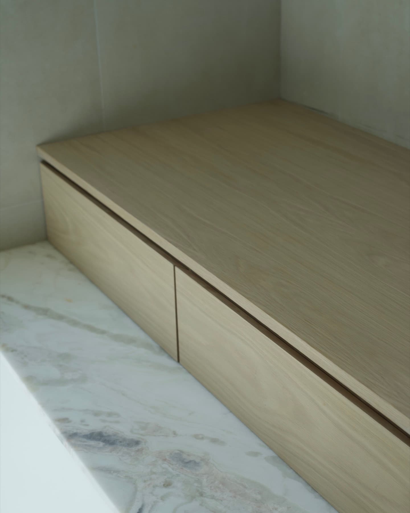 Built-in white oak bench with push-latch drawers beside a marble curb in a bathroom