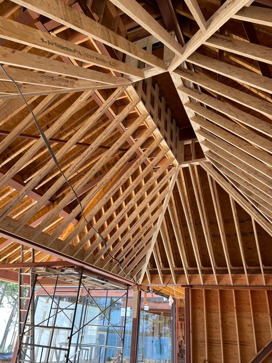 Upward view of complex timber roof framing with engineered lumber joists radiating from a steel beam inside a house under construction