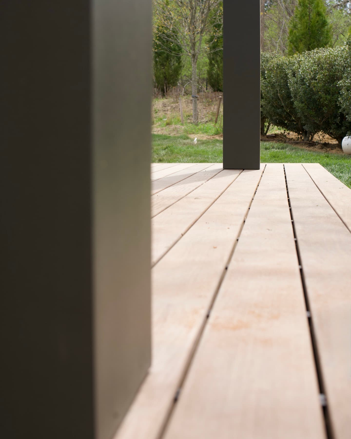 Low view across new ipe wood decking between dark painted porch columns, with lawn and hedges beyond