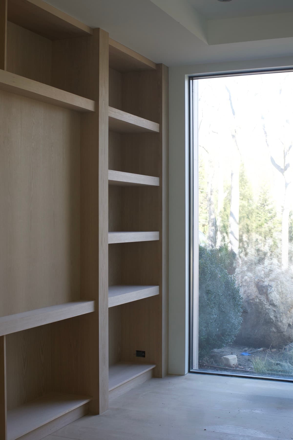 Floor-to-ceiling white oak shelving built around a full-height window looking into greenery